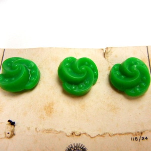 May include: Three green plastic buttons with a swirl design. The buttons are on a white card with the number 118/24 printed on it.