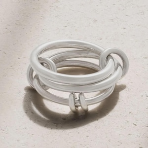 Könnte beinhalten: Ein silberfarbener Ring mit einem einzigartigen, ineinandergreifenden Design. Der Ring verfügt über mehrere abgerundete Bänder, die sich verschlingen und einen modernen und stilvollen Look erzeugen. Das Metall hat eine glatte, polierte Oberfläche.