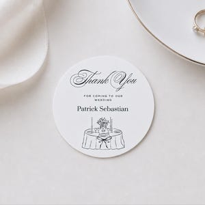 May include: A circular white card featuring black text that reads Thank You FOR COMING TO OUR WEDDING Patrick Sebastian, with a line drawing of a table setting including a floral centerpiece, candles, and a tablecloth with a bow.