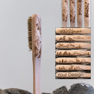 Könnte beinhalten: Eine helle Holzkletterbürste mit Naturborsten und einer lasergravierten Darstellung einer Person beim Bergsteigen. Das Bild enthält eine Collage verschiedener Gravuroptionen, darunter Blumen, Tiere und der Schriftzug Your Design.