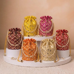 May include: Six drawstring pouches in yellow, magenta, dark red, orange, gold, and red, each featuring a diamond-patterned fabric with small circular mirrors and gold embroidery. Every pouch includes a white pearl-beaded handle and drawstring.