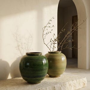 以下が含まれることがあります： 光沢のある仕上げの丸い陶器製の花瓶が2つ。1つは水平な帯模様が入った深いフォレストグリーンで、もう1つは質感のあるリブ状の表面を持つ明るいオリーブグリーンです。オリーブグリーンの花瓶には、小さな葉がついた細い枝が挿されています。