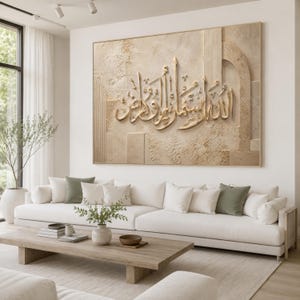 May include: A large rectangular wall art piece featuring raised gold Arabic calligraphy centered on a textured beige background. The artwork incorporates geometric shapes and layered panels, creating a three-dimensional effect with a neutral color palette.