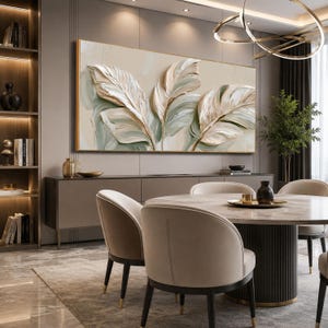 May include: A large rectangular wall art piece featuring a textured, impasto-style painting of three oversized leaves in shades of cream, beige, and sage green. The artwork is framed in a thin gold border and displayed horizontally above a sideboard.