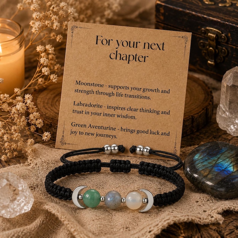 May include: A black cord bracelet featuring three round gemstone beads in green, grey, and white, flanked by two silver-toned crescent moon charms. The bracelet is displayed on a tan card with the text For your next chapter and descriptions of Moonstone, Labradorite, and Green Aventurine.