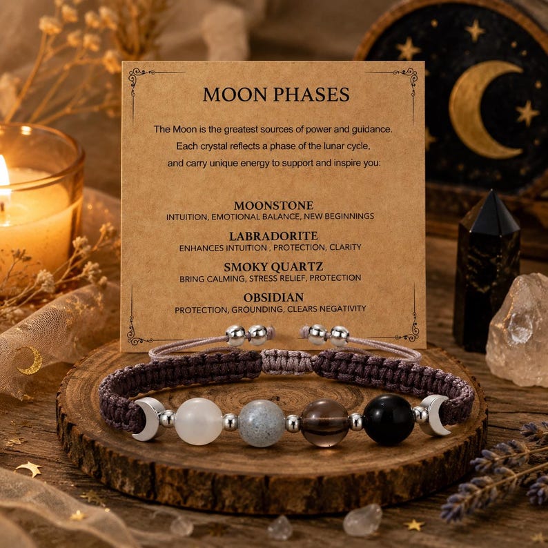 May include: A brown woven cord bracelet featuring four spherical beads in white, grey, brown, and black, accented by two silver-toned crescent moon charms. The bracelet is displayed in front of a tan card printed with the text MOON PHASES.