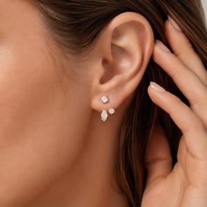 May include: A set of three gold-toned stud earrings featuring clear, faceted stones. The top earring is a round solitaire, while the lower pair consists of one small round solitaire and one marquise-cut stone, all secured with metal prongs.