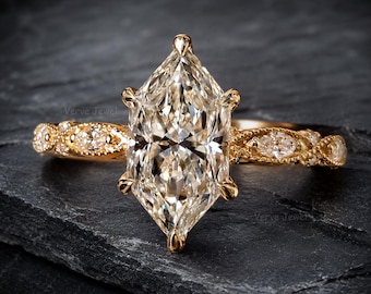 May include: A gold ring featuring a large marquise-cut center stone held by six prongs. The band is crafted with a decorative milgrain edge and is set with smaller marquise-cut stones along the sides, creating a detailed and intricate appearance.