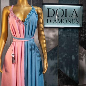 Pu&ograve; includere: Abito bicolore rosa e blu su manichino. L'abito presenta dettagli floreali sulle spalline e una cintura abbinata. L'insegna dietro il manichino recita "DOLA DIAMONDS".