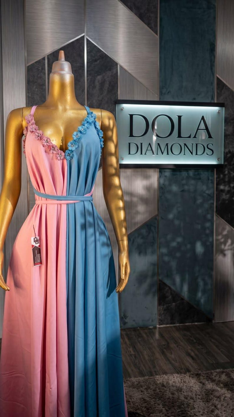 Pu&ograve; includere: Abito bicolore rosa e blu su manichino. L'abito presenta dettagli floreali sulle spalline e una cintura abbinata. L'insegna dietro il manichino recita "DOLA DIAMONDS".