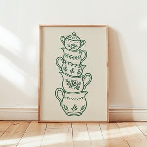 以下が含まれることがあります： ダークグリーンの線画で描かれた5つのクリーム色の陶器が垂直に積み重なったデザインの額入りウォールアートプリント。蓋付きのシュガーボウルと4つの異なるピッチャーが描かれており、それぞれに花や葉の模様が施されています。