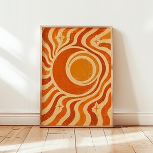 May include: A rectangular wall art print featuring a central orange sun and crescent moon motif surrounded by wavy, radiating lines in shades of orange, yellow, and cream. Four small, four-pointed star shapes are positioned in the corners.