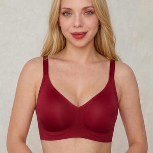Può includere: Un reggiseno color rosso scuro a tinta unita con una struttura liscia e senza cuciture, coppe modellate, una fascia sottoseno ampia per il sostegno e spalline regolabili. Il design è semplice, privo di motivi, pizzi o decorazioni visibili.
