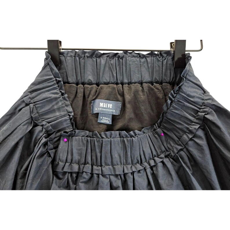 Puede incluir: Falda negra con cintura fruncida y silueta amplia y fluida. La falda est&aacute; colgada de una percha negra. La etiqueta dice "Maeve by Anthropologie". La falda es talla X-Small.