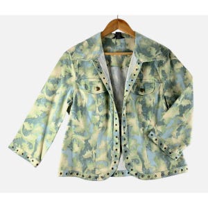 May include: A light-colored jacket with a unique pattern of green, blue, and cream swirls. The jacket has a collared neckline, two chest pockets, and three-quarter sleeves. It features metal stud detailing along the edges and button closures.