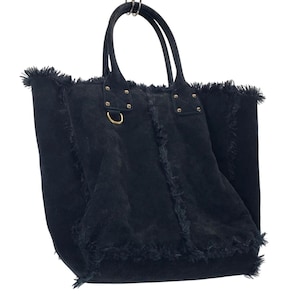 May include: A black tote bag with a fringed edge and two handles. The bag has gold-colored rivets and a gold-colored ring on the side. The bag is made of a soft, textured material.