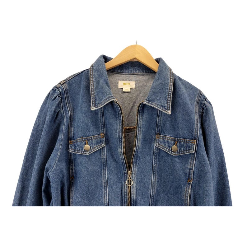 May include: A mid-wash denim jacket with a zip-up front, two chest pockets with button fastenings, and a collared neckline. The jacket is hanging on a wooden hanger. The brand name "WEVE" is visible on the inside of the collar.