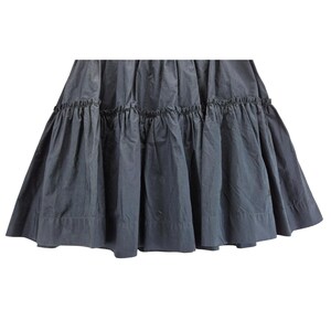 Puede incluir: Falda gris oscuro con un dise&ntilde;o escalonado y con volantes. La falda tiene una silueta completa y fluida, con m&uacute;ltiples capas de tela que crean volumen y movimiento. La tela parece ser un material ligero, adecuado para climas c&aacute;lidos.