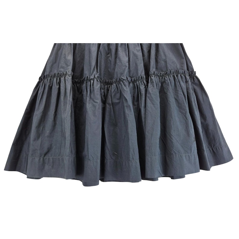 Puede incluir: Falda gris oscuro con un dise&ntilde;o escalonado y con volantes. La falda tiene una silueta completa y fluida, con m&uacute;ltiples capas de tela que crean volumen y movimiento. La tela parece ser un material ligero, adecuado para climas c&aacute;lidos.