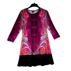 Könnte beinhalten: Langärmliges Kleid mit einem lebendigen Paisley-Muster in Lila, Orange und Türkis. Das Kleid hat einen schwarzen Saum und hängt an einem schwarzen Kleiderbügel. Das Kleid ist in Größe S.