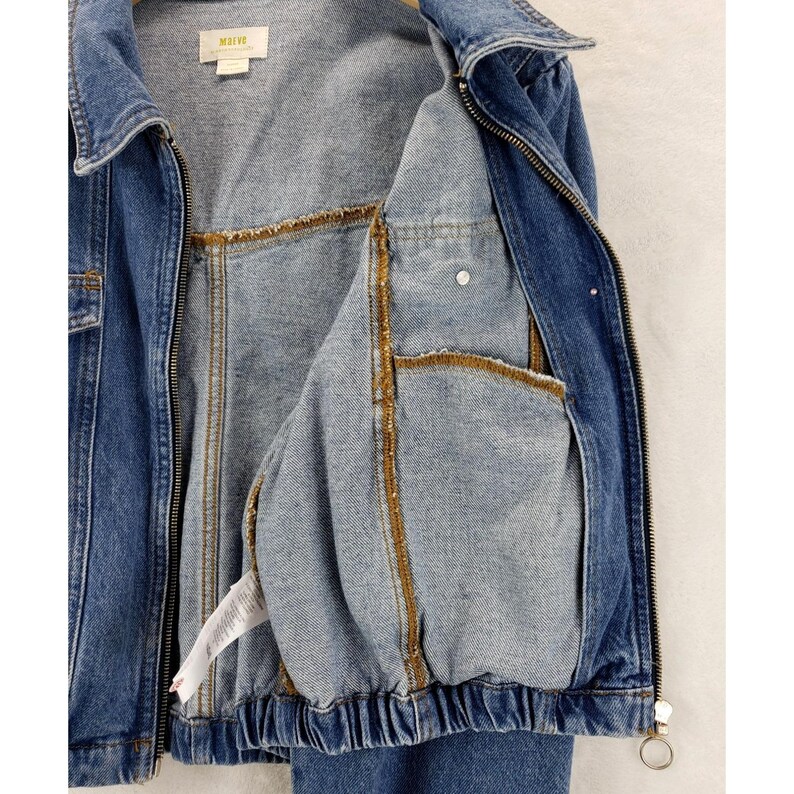 May include: A blue denim jacket with a zip fastening and a collared neckline. The jacket has two front pockets and a light blue interior with gold-coloured stitching. The jacket has a label that reads "MAEVE".