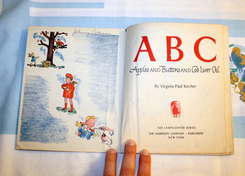 May include: A vintage children's book titled "ABC Apples and Buttons and Cod Liver Oil" by Virginia Paul Kircher. The cover features a red, white, and blue illustration of a child holding an apple.