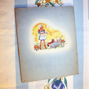 May include: A vintage children's book illustration featuring a young girl dressed as a nurse, holding a bottle and standing next to a small bed with a dog and a cat inside. The illustration is on a light blue background.