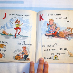 May include: An open children's book with colorful illustrations. The left page features the letter J and the word "Jumping ropes". The right page features the letter K and the word "Kittens".