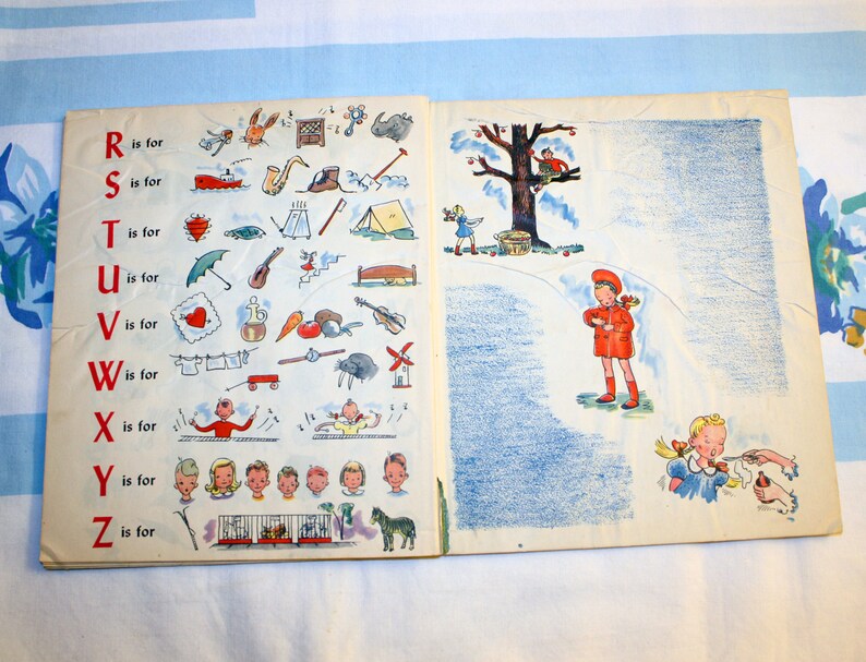 May include: An open book with colorful illustrations of the alphabet and objects starting with each letter. The book is open to the page with the letters R, S, T, U, V, W, X, Y, and Z. The illustrations include a rabbit, a ship, a tent, an umbrella, a vase, a wagon, a xylophone, a yo-yo, and a zebra.