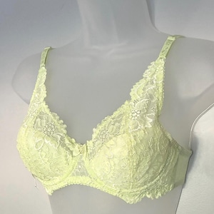May include: A pale yellow lace bra featuring floral patterns, adjustable shoulder straps, and a small decorative bow at the center gore. The garment is constructed with underwire cups and scalloped lace edges along the neckline and underband.