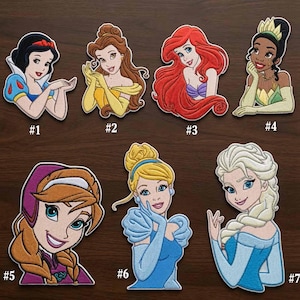 Può includere: Una collezione di sette toppe ricamate raffiguranti personaggi dei cartoni animati. Ogni toppa è numerata da #1 a #7 e mostra varie figure con diversi colori di capelli, espressioni facciali e stili di abbigliamento in colori vivaci.