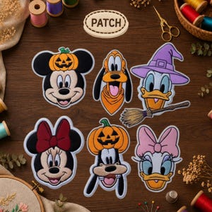 May include: A collection of six embroidered patches featuring Disney characters. The set includes Mickey Mouse with a pumpkin, Pluto, Donald Duck as a witch with a broom, Minnie Mouse with a red bow, Goofy with a pumpkin, and Daisy Duck with a pink bow.