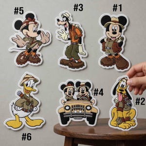 May include: Six embroidered patches featuring Disney characters in safari gear. #1 shows Mickey Mouse, #2 Pluto, #3 Goofy, #4 Minnie and Mickey in a jeep, #5 Minnie Mouse, and #6 Donald Duck. Each patch has a white border and detailed stitching.