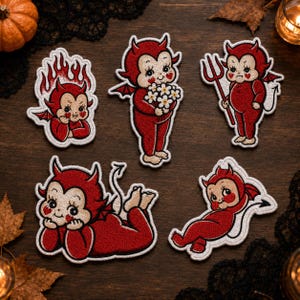May include: Five embroidered patches featuring red devil characters with pale faces and heart-shaped cheeks. The designs include a devil in flames, one holding white flowers, one with a pitchfork, one lying down, and one in a reclining pose.