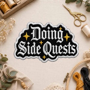 May include: An embroidered patch with a black background and white text that reads Doing Side Quests in a gothic font. The patch features small yellow four-pointed star accents and a white border, designed for application to fabric items.