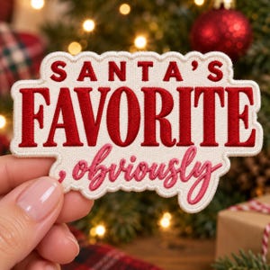 Puede incluir: Un parche bordado de color crema con borde festoneado que presenta el texto rojo SANTA'S FAVORITE y el texto cursivo rosa ,obviously. El parche tiene un acabado de hilo denso y texturizado con una forma irregular que sigue las letras.