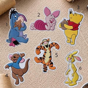 Puede incluir: Seis parches bordados termoadhesivos con personajes de dibujos animados: Igor con un muñeco, Piglet tumbado, Winnie the Pooh con un tarro de miel, Rito, Tigger saltando y Conejo. Cada parche está numerado del uno al seis sobre un fondo texturizado.