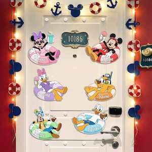 May include: A white door decorated with six Disney character cutouts, each featuring a character in a pool float with the word Name printed on it. Characters include Minnie, Mickey, Daisy, Pluto, Goofy, and Donald. String lights with anchors and life rings frame the door.