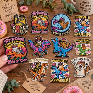 May include: A collection of embroidered patches featuring cats and dinosaurs in various colourful designs. The patches include text such as Princess Donut & Mongo, Ride or Roar, Outrage Awaits, Mongo is Appalled, and I am Yelling Carl, with vibrant illustrations of cats riding dinosaurs.