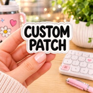 May include: A white embroidered patch with a scalloped edge featuring the text CUSTOM PATCH in bold black lettering. The patch has a clean white background and a thick black border, designed for application onto fabric surfaces as a decorative element.