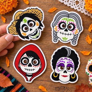 Può includere: Quattro toppe ricamate raffiguranti volti di teschi stilizzati con intricati dettagli colorati. Un teschio indossa un cappello di paglia, uno ha capelli grigi intrecciati, uno indossa un cappuccio rosso e uno ha capelli neri con accenti viola e orecchini d'oro.