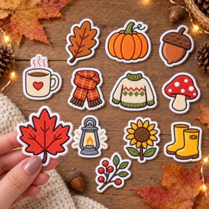 Könnte beinhalten: Eine Sammlung bestickter Aufnäher mit herbstlichen Motiven, darunter ein rotes Ahornblatt, ein orangefarbener Kürbis, eine braune Eichel, eine Kaffeetasse mit Herz, ein karierter Schal, ein Pullover, ein roter Pilz, eine Laterne, eine Sonnenblume und gelbe Stiefel.