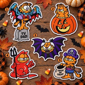 May include: Five embroidered patches featuring the orange cat Garfield in Halloween costumes: a vampire on a tombstone labeled TV DAD, a cat in a jack-o'-lantern, a bat, a devil with a pitchfork, and a pirate holding a bag labeled TRICK OR TREAT.