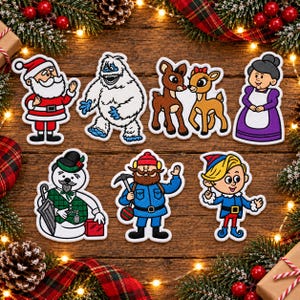 Peut inclure: Un ensemble de sept écussons brodés représentant des personnages de Noël, dont le Père Noël, un yéti, deux rennes, la Mère Noël, un bonhomme de neige avec un haut-de-forme et un parapluie, un explorateur barbu avec un pic et un elfe blond.