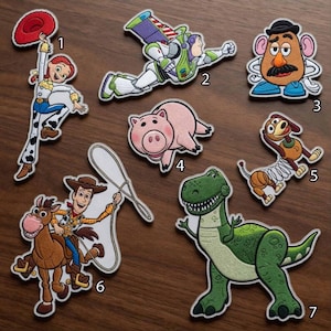 May include: A collection of seven embroidered patches featuring characters from Toy Story, numbered one through seven. The patches depict Jessie, Buzz Lightyear, Mr. Potato Head, Hamm, Slinky Dog, Woody riding Bullseye, and Rex the green dinosaur.