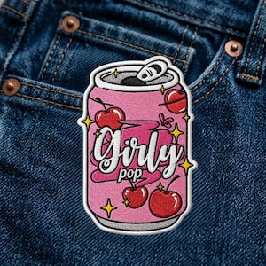 Puede incluir: Un parche bordado con forma de lata de refresco rosa que presenta el texto Girly pop en letra cursiva blanca. El diseño incluye cerezas rojas con tallos verdes y estrellas amarillas de cuatro puntas sobre un fondo rosa texturizado.