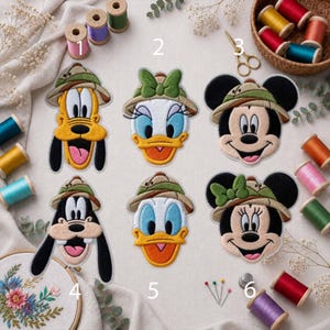 May include: Six embroidered patches featuring cartoon characters wearing safari hats, arranged in two rows. The characters include Pluto, Daisy Duck, Mickey Mouse, Goofy, Donald Duck, and Minnie Mouse. The patches are surrounded by colorful thread spools.