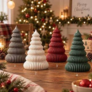 Peut inclure: Quatre décorations de sapin de Noël coniques avec un design nervuré et superposé. Les arbres sont de couleur gris foncé, crème, rouge profond et vert forêt, chacun marqué d'un petit chiffre de un à quatre sur une surface en bois.