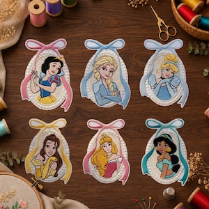 Pode incluir: Seis emblemas bordados ovais com princesas de desenhos animados, cada um emoldurado por uma borda decorativa e um laço. Os emblemas mostram a Branca de Neve, Elsa, Cinderela, Bela, Aurora e Jasmine com seus trajes e penteados.