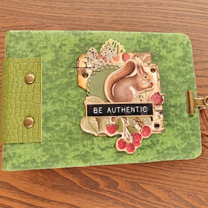 Könnte beinhalten: Ein mit grünem Stoff bezogenes Journal mit einem strukturierten grünen Buchrücken und zwei Messingnieten. Das Cover zeigt eine Collage mit einer Eichhörnchen-Illustration, roten Himbeeren und einem schwarzen Etikett mit dem Text BE AUTHENTIC.